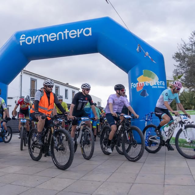 Ciclistas en la salida bajo el arco azul de Formentera